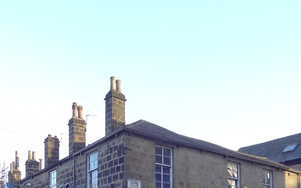 Gable end of a stone terrace in Leeds with chimney pots above a slate roof